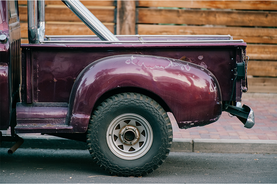 Närbild på bakpartiet på en äldre, lila bil med flak.
