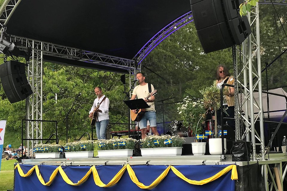 Tre personer i vita tröjor och varsin gitarr uppträder på en scen