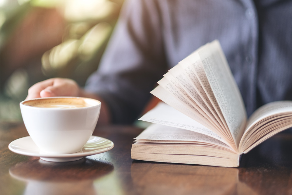 Bild på en uppslagen bok och en kopp rykande kaffe.