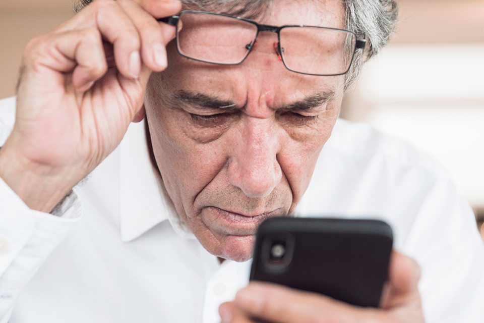 Äldre bekymrad man skjuter upp glasögonen i pannan och tittar på telefonen