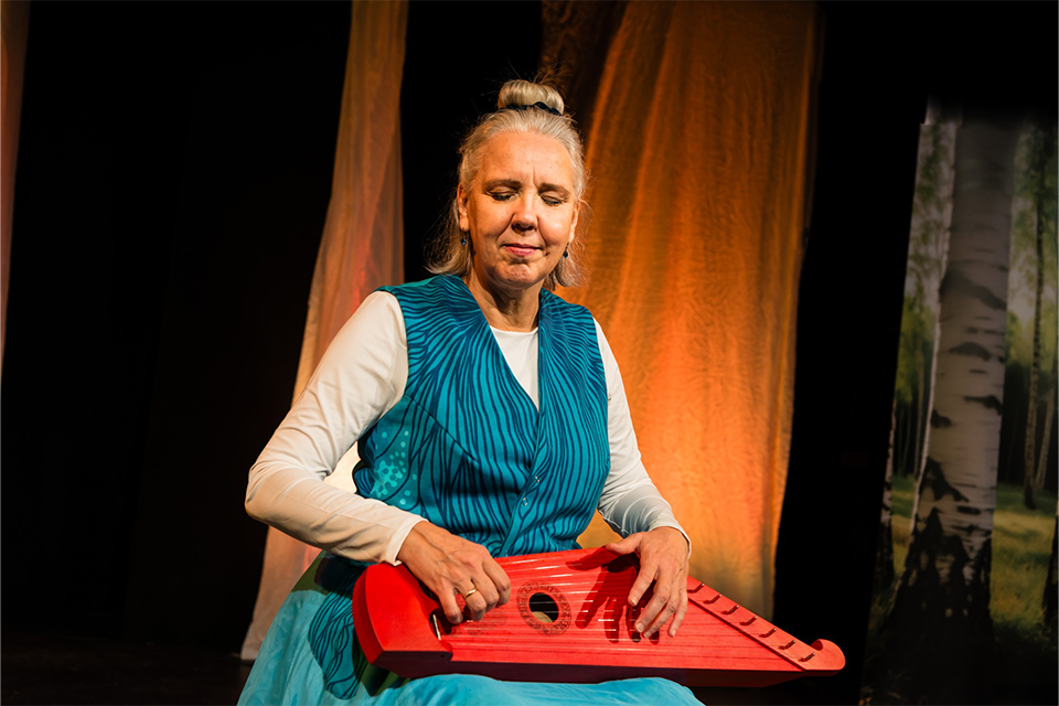 Kvinna på en scen spelar ett stränginstrument hon har i knäet.