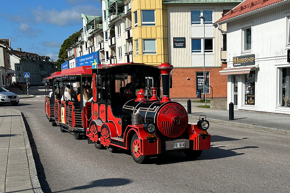 Turisttåg kör på Järnvägsgatan en solig dag. Tåget är rött och svart.