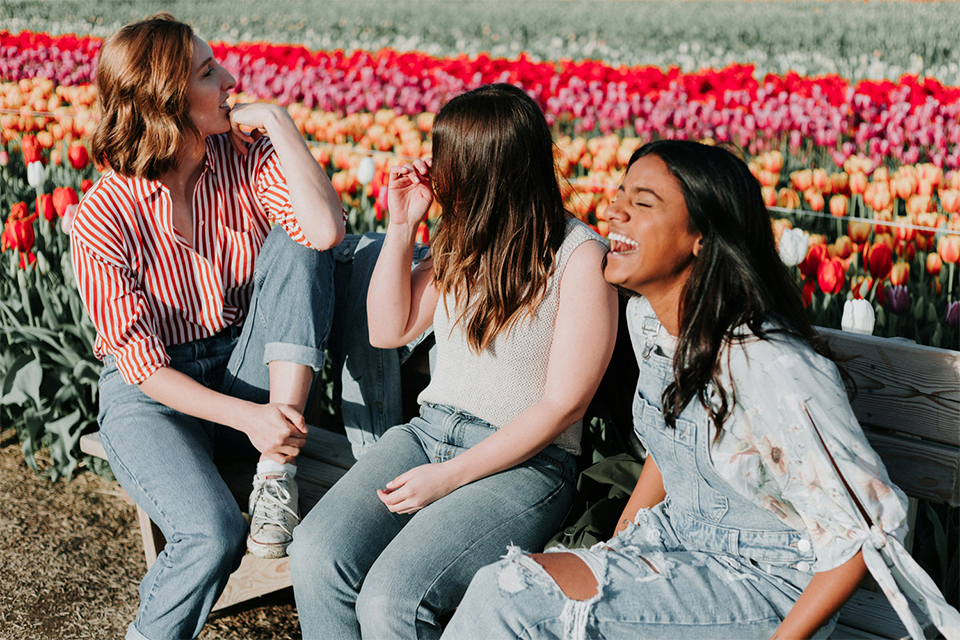 Tre glada tjejer sitter på en parkbänk. I bakgrunden tulpaner.