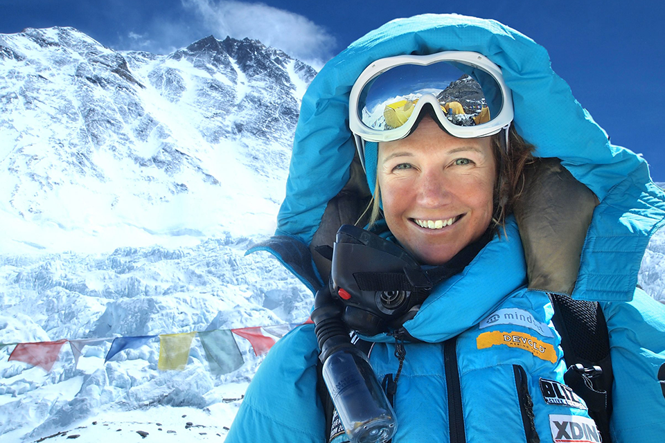 Äventyraren Annelie Pompe klädd i bergsbestigarutrustning. I bakgrunden höga berg och blå himmel.