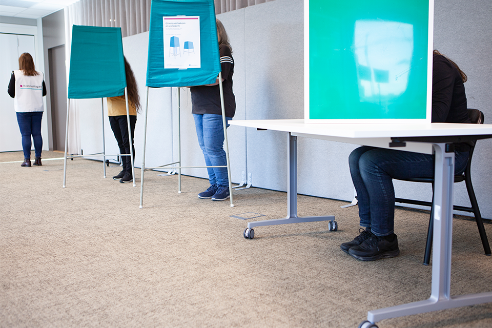 tre personer bakom valskärmar. En valarbetare i bakgrunden.