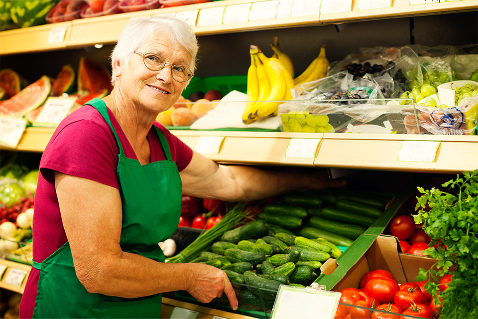 Bild visar kvinna vid grönsaksdisk i butik.
