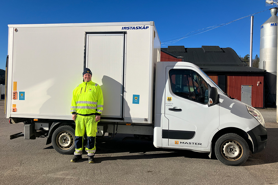 Man med neongula ärbetskläder framför en vit liten lastbil