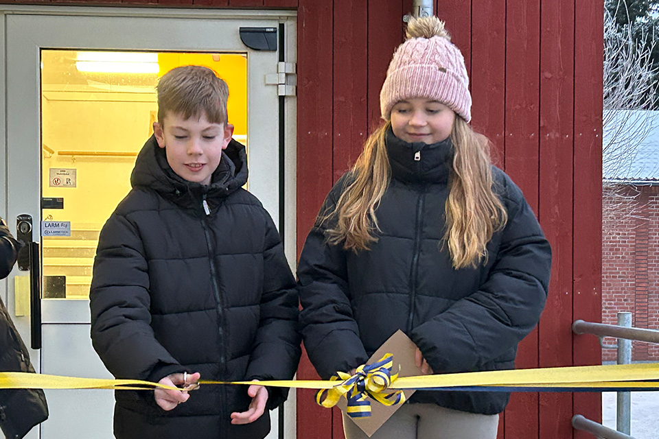 Två elever i vinterkläder klipper ett invigningsband utomhus.