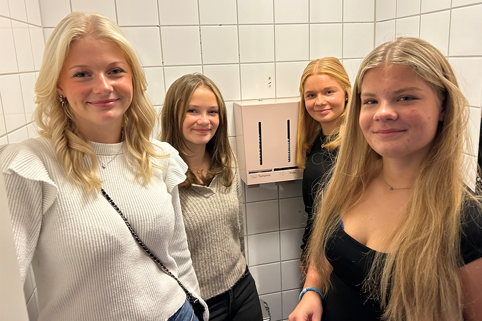 Fyra elever, tjejer, i årskurs nio inne på en toalett med en automat i mitten.