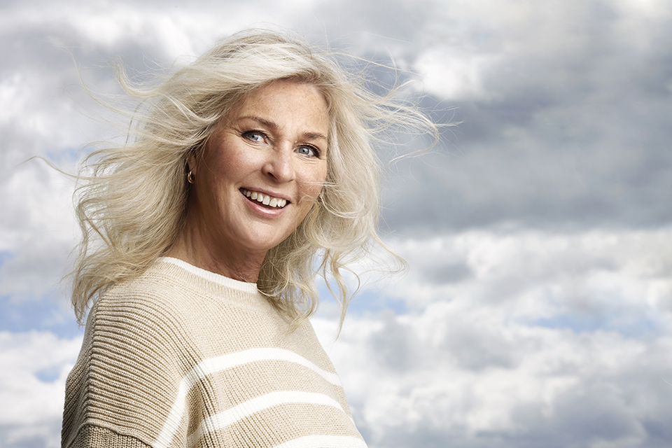 Bild på en leende Åsa Hellberg mot blå sommarhimmel med små moln.