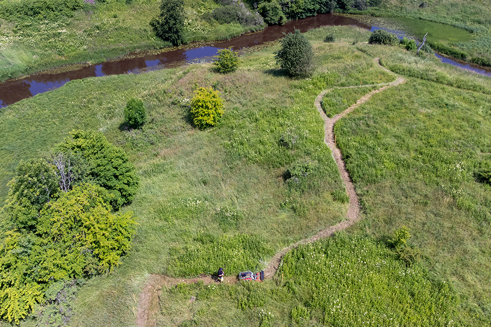Flygbild som visar ett klippt gångstråk i naturen intill en å.