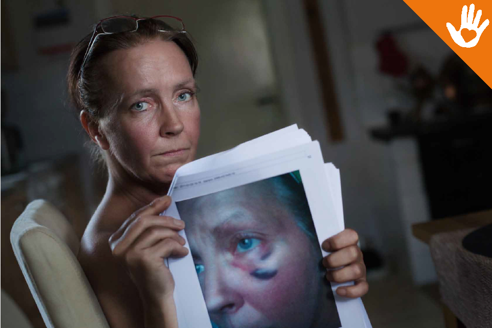 Bilden visar en kvinna som håller upp en bild på sig själv som visar hur hon sett ut efter att ha blivit misshandlad.