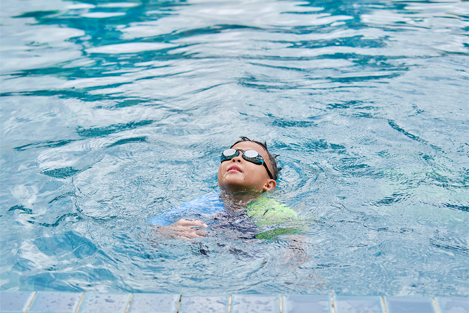 Ung kille med simglasögon simmar vid en brygga
