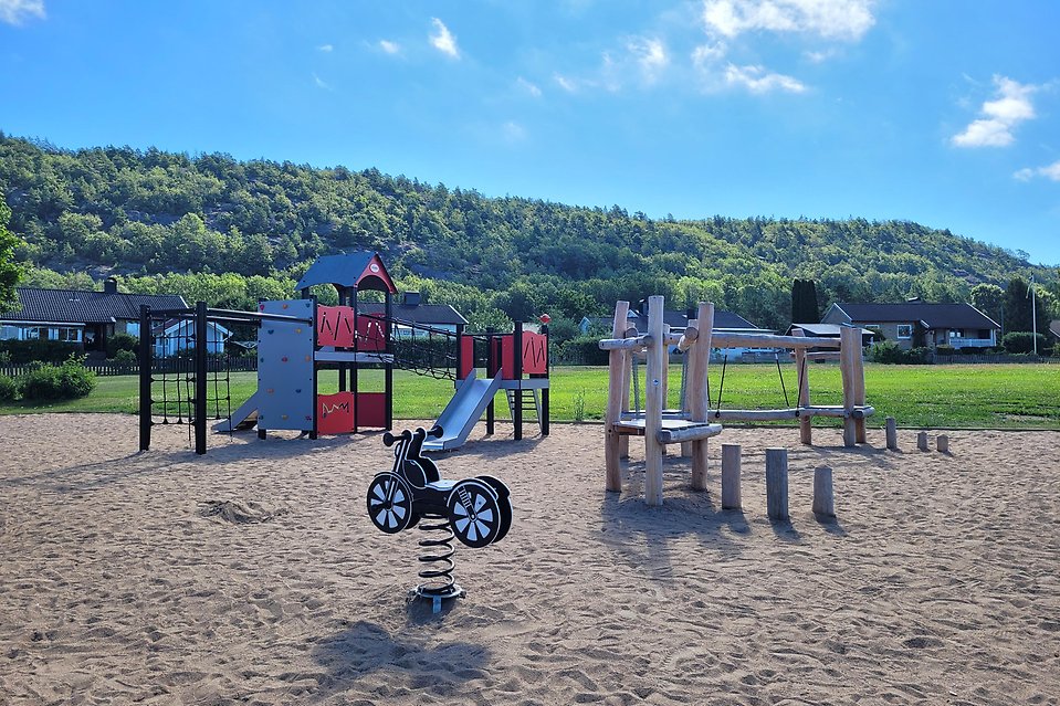 Bild från lekplats med stor klätterställning med rutchelkana, motorcykelgunga och balanshinder i trä