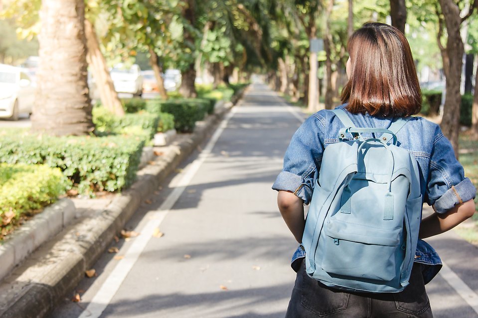 Tonåring går längs en gata med en blå ryggsäck på ryggen