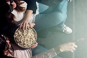 Två kvinnor sitter i en biosalong och äter popcorn. Bild tagen uppifrån.