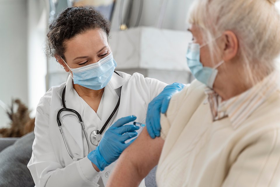 En sjukvårdare med munskydd ger en kvinna en spruta i armen