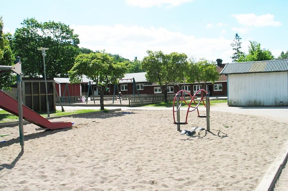 Lekplats med rutchelkana i förgrunden och röd byggnad i bakgrunden