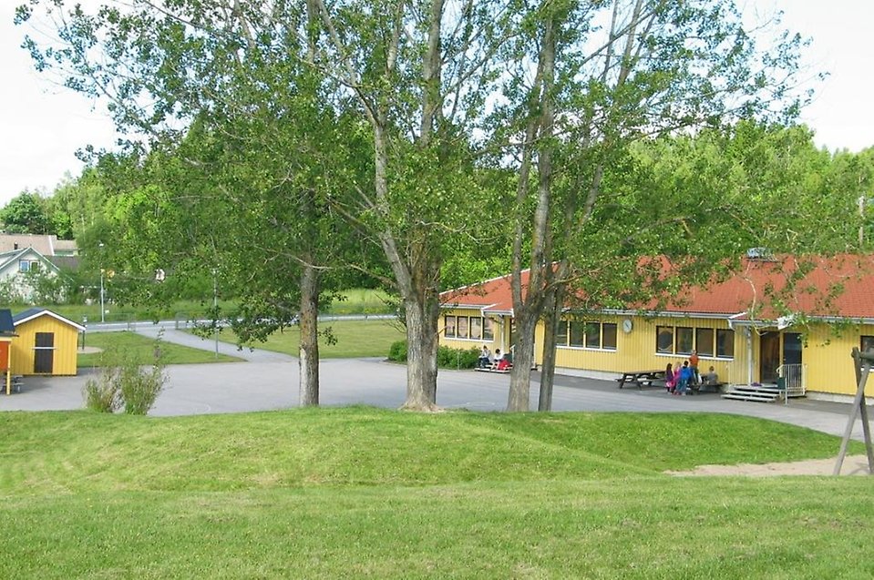 Bild på en gul byggnad med träd och gräsmatta framför