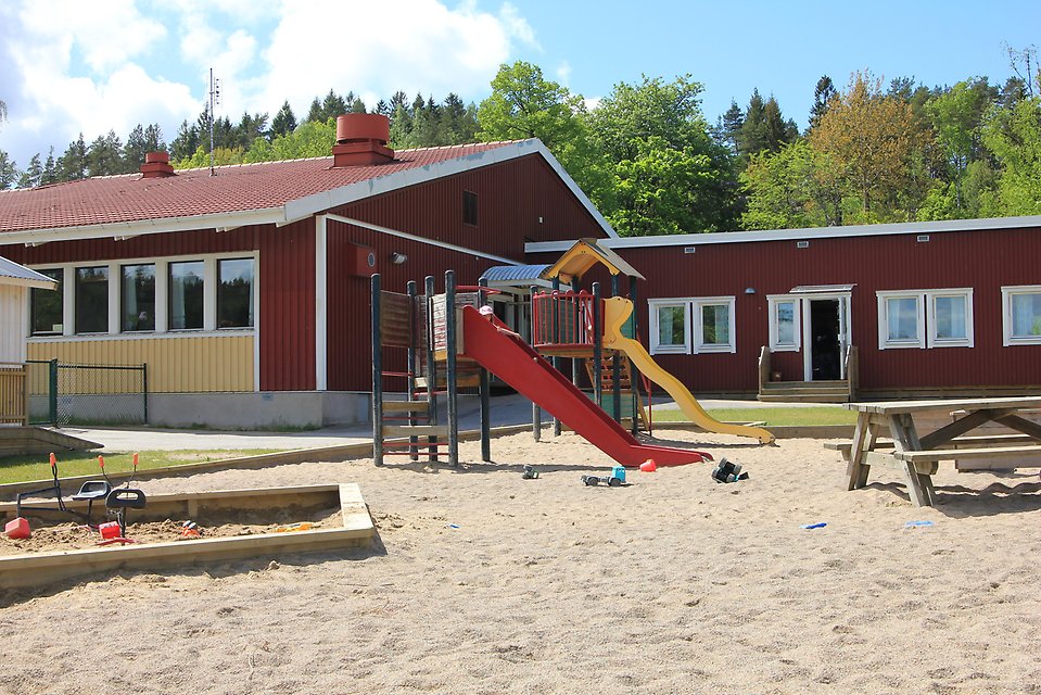 En röd byggnad med stor sandlåda och lekplats framför.