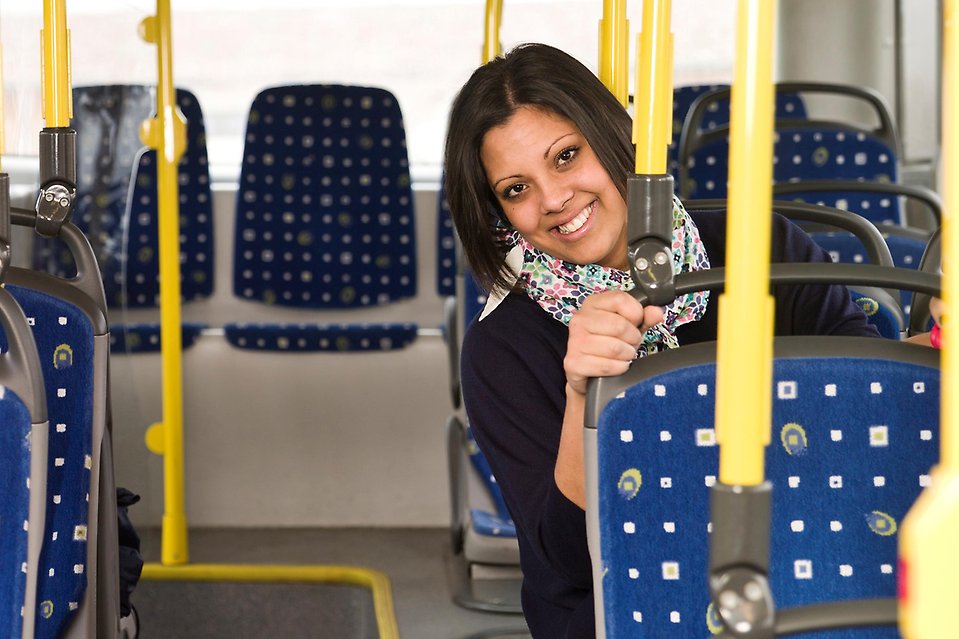 En kvinna med mörka kläder och mörk hår sitter på bussen och håller i sätet framför sig.