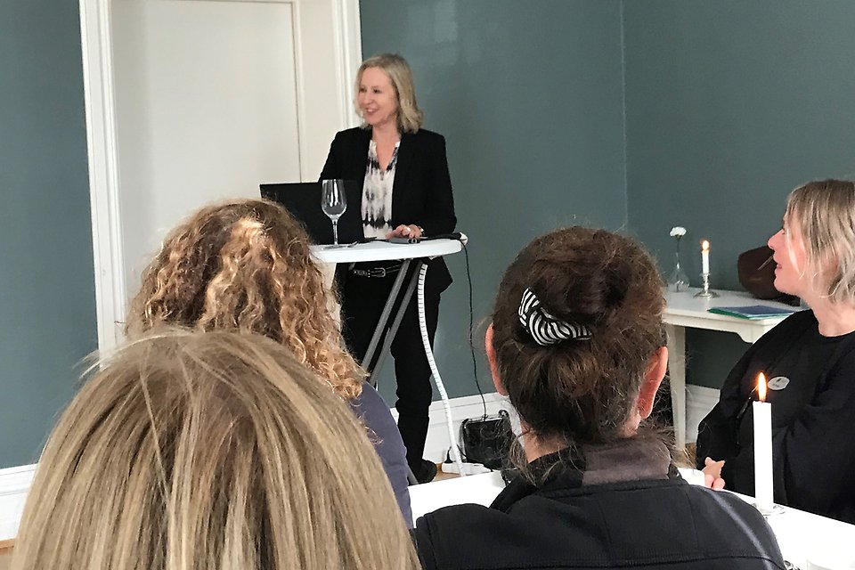 Christina Riksén, Svenskt Näringsliv, står och talar vid ett ståbord. Personer bakifrån syns i förgrunden.