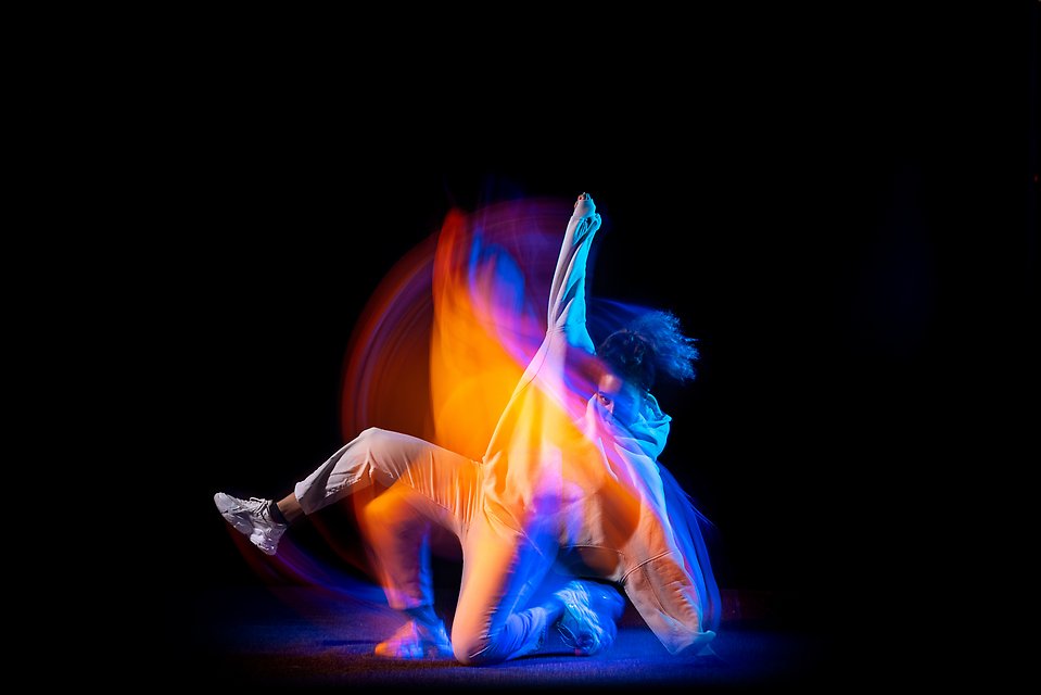 Dansare mot svart bakgrund. Effektfull och färgstark bild där man ser rörelsen.