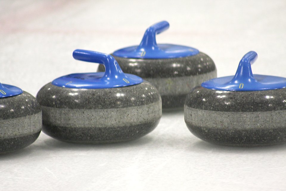 Fyra curlingklot med blått handtag på en isbana