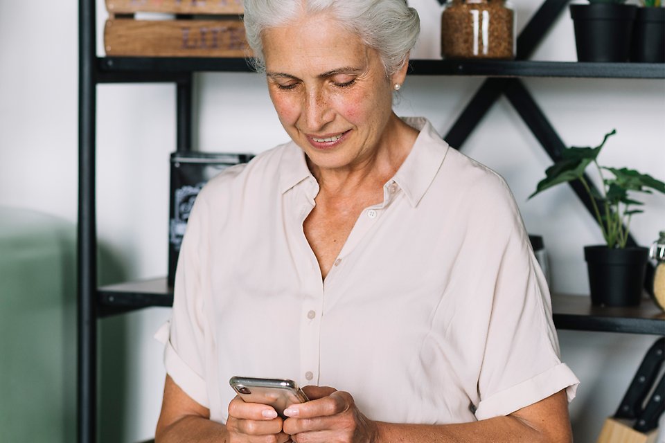 Äldre kvinna i vit blus håller i en smartphone