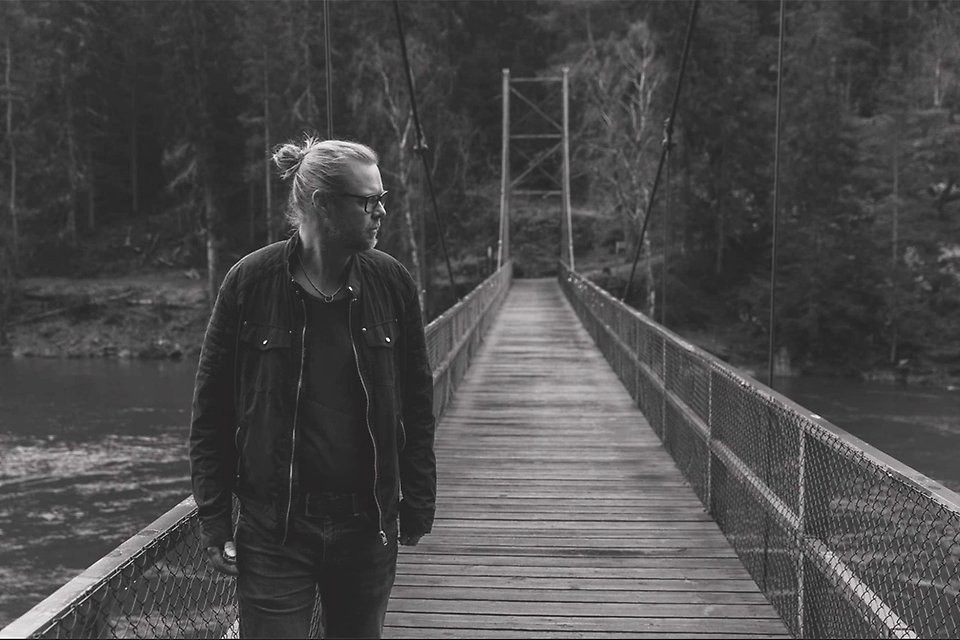 En svartvit bild på en man i långt hår och tofs som går på en bro